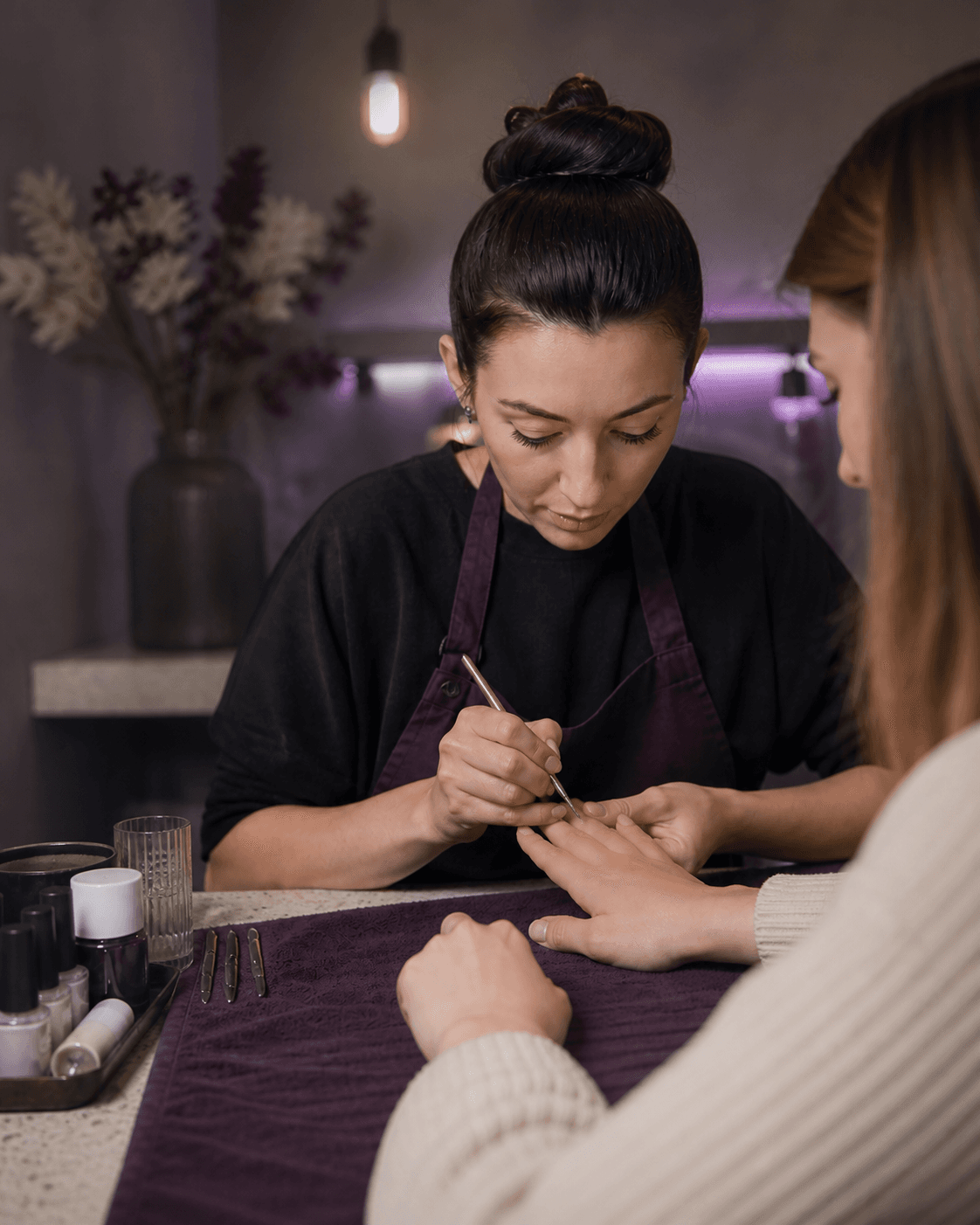 A nail artist concentrating on the finishing details of a client’s manicure